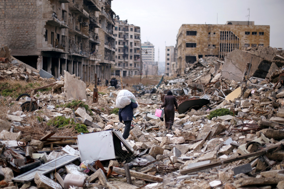 People walk amid the rubble as they carry belongings that they collected from their houses in the government controlled area of Aleppo, Syria, on Saturday.