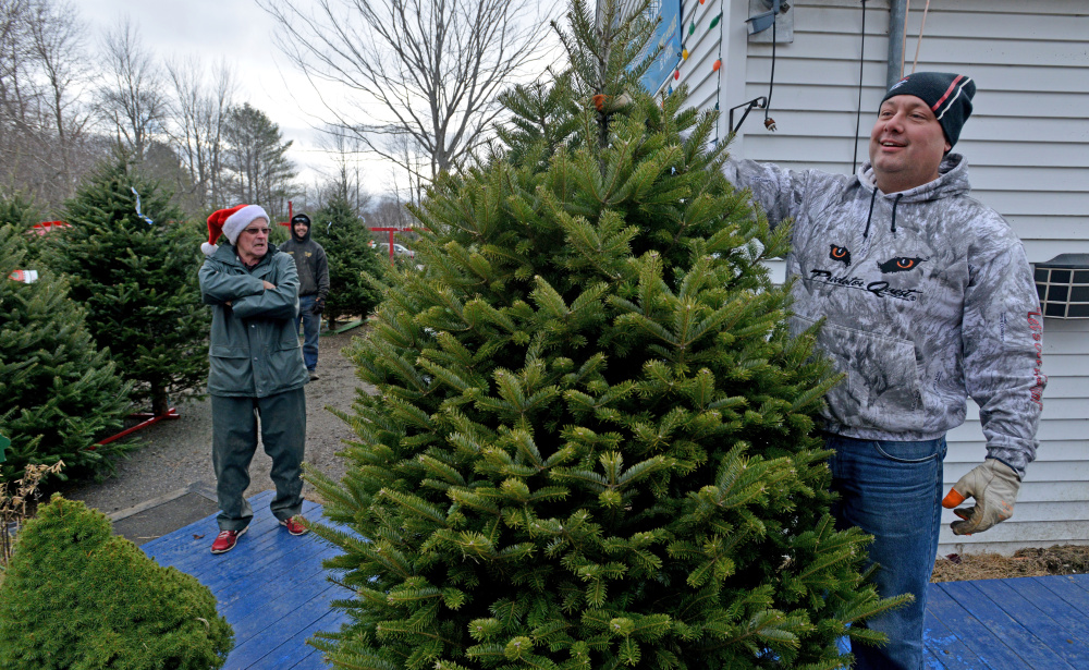 Scott Knight stands with his new Christmas tree Saturday as Bryant LaPlante, owner of The Forest, a Christmas tree farm in Cornville, stands in the back.