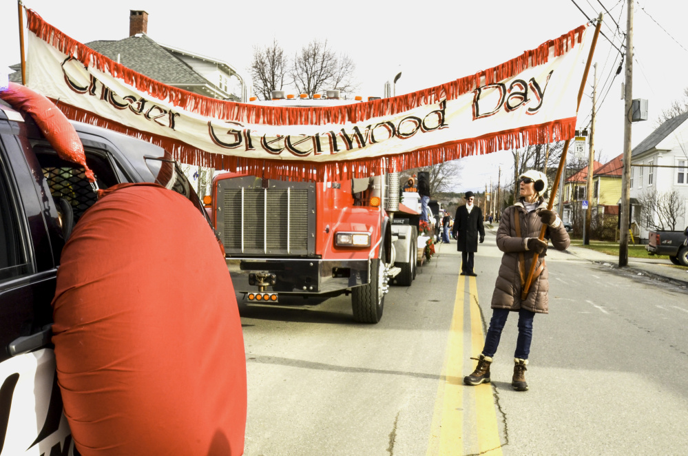 A woman readies a banner Saturday in Farmington as the 40th Chester Greenwood gets underway, honoring the inventor of earmuffs. In back, donning a black coat, hat and the trademark earmuffs, is Clyde Ross, who portrays Greenwood every year during the parade.