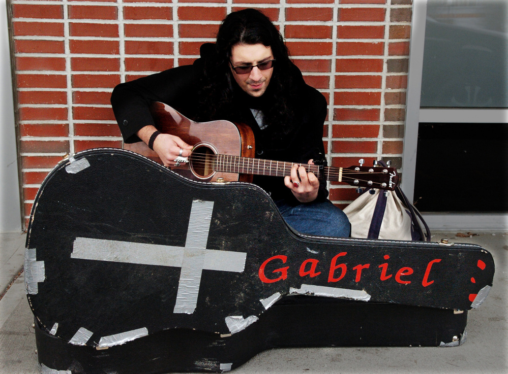 Michael Pastore sings and plays his guitar he calls Gabriel on the sidewalk outside of the Chapter 11 store in Waterville on a cold Wednesday.