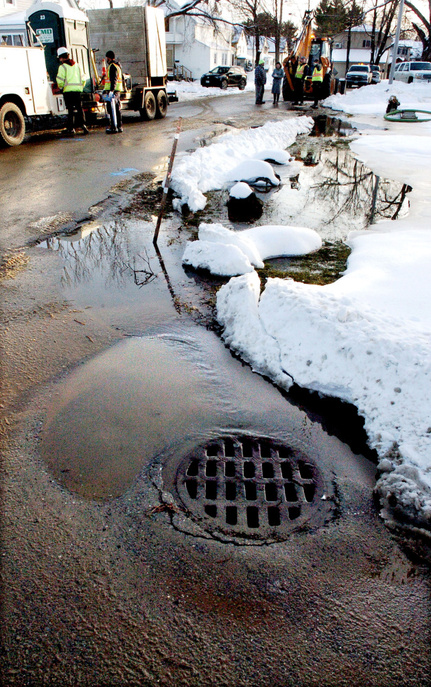 Workers with Kennebec Water District wait for clearance to begin digging to repair a water main break as surface water runs into a drain on Broad Street in Waterville on Tuesday.