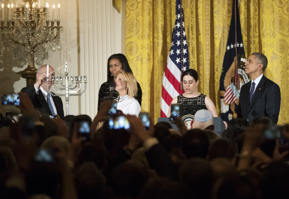Rachel Isaacs, second from right, rabbi at Colby College and of Beth Israel Congregation in Waterville, gave the invocation at Wednesday night's White House Hanukkah reception. With the invocation over, Chemi Peres, left, and Mika Almog, at left and second from left in front, son and granddaughter of former President of Israel Shimon Peres, light the Menorah while first lady Michelle Obama, behind Almog, and President Barack Obama, right, watch during a reception in the East Room of the White House in Washington.