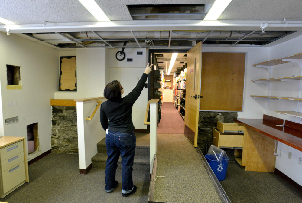 Tammy Rabideau, assistant director at the Waterville Public Library, points on Saturday to a pipe that broke overnight in the library. Water spilling from the pipe damaged books and computers the library.