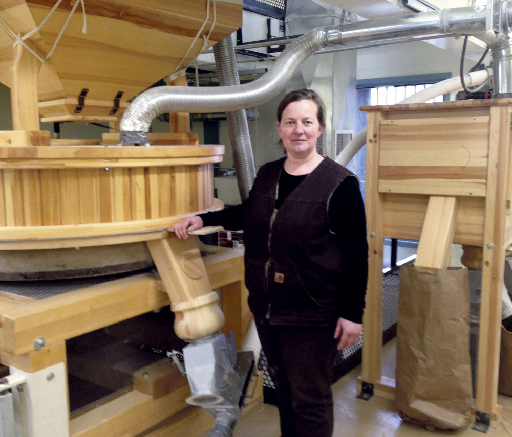 Amber Lambke stands beside a working mill while grinding flour in 2014 at the Somerset Grist Mill in Skowhegan. Lambke is president of Maine Grains.