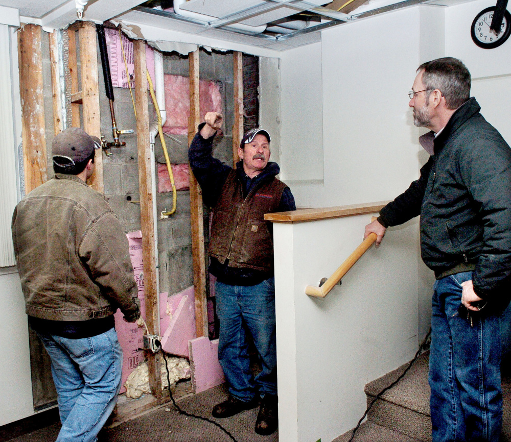 Waterville City Engineer Greg Brown, right, confers on Thursday with Houle's Plumbing Heating & Air Conditioning employees Evan Thurlow, left, and Frank Lizotte near an opened wall at the Waterville Public Library, where cold air seeped into the library last weekend and froze a water pipe, causing it to burst and inflict serious damage on books and equipment.
