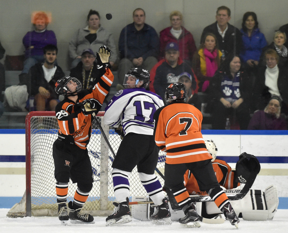 Winslow's Tyler Martin, left, tries to swat the puck out of the air as Waterville's Cooper Hart (17) looks for the rebound Tuesday at Colby College in Waterville.