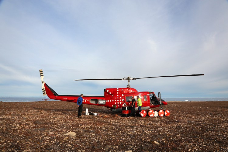 Members of the crew refuel the helicopter at a spot where they had left fuel on a previous trip in anticipation of this one. 