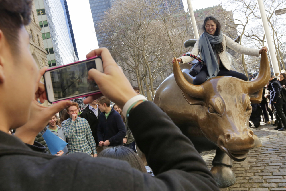People pose with "Charging Bull," a bronze sculpture by Arturo Di Modica, in New York's Financial District, Wednesday. The Dow Jones industrial average closed over 20,000 points for the first time, the latest milestone in a record-setting drive for the stock market.