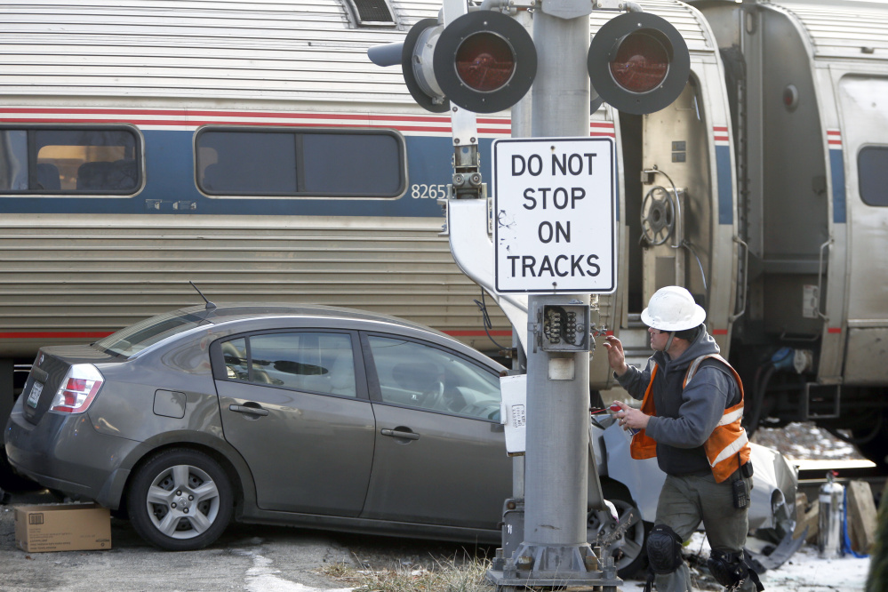A repairman works on the railroad crossing signal on Brighton Avenue after Friday's crash. Police say the Nissan Sentra collided with the Downeaster when the driver tried to outrace the train.