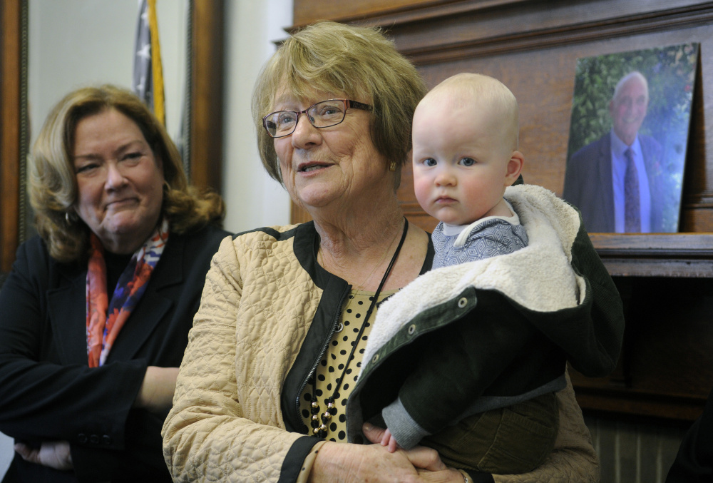 Libby Mitchell addresses guests while holding her grandson, West Mitchell, after her inauguration Tuesday as Kennebec County Judge of Probate in Augusta. At left is Maine Supreme Court Chief Justice Leigh Saufley. At right is a photo of her late husband, James Mitchell, who served as probate judge for 37 years.