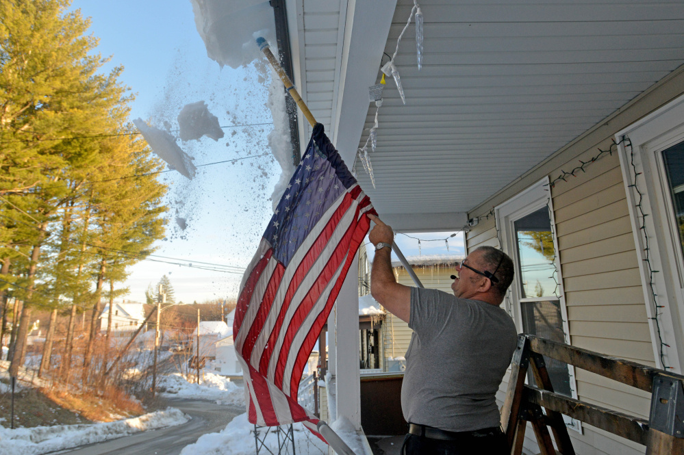 Richard Perkins clears his new porch roof from hanging snow and ice Thursday at his residence on Redington Street in Waterville.