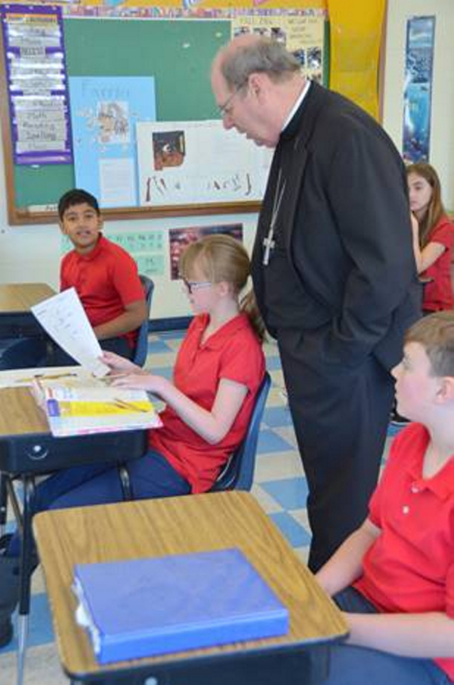 Kya Douin shows Bishop Robert P. Deeley her work during a recent classroom visit.