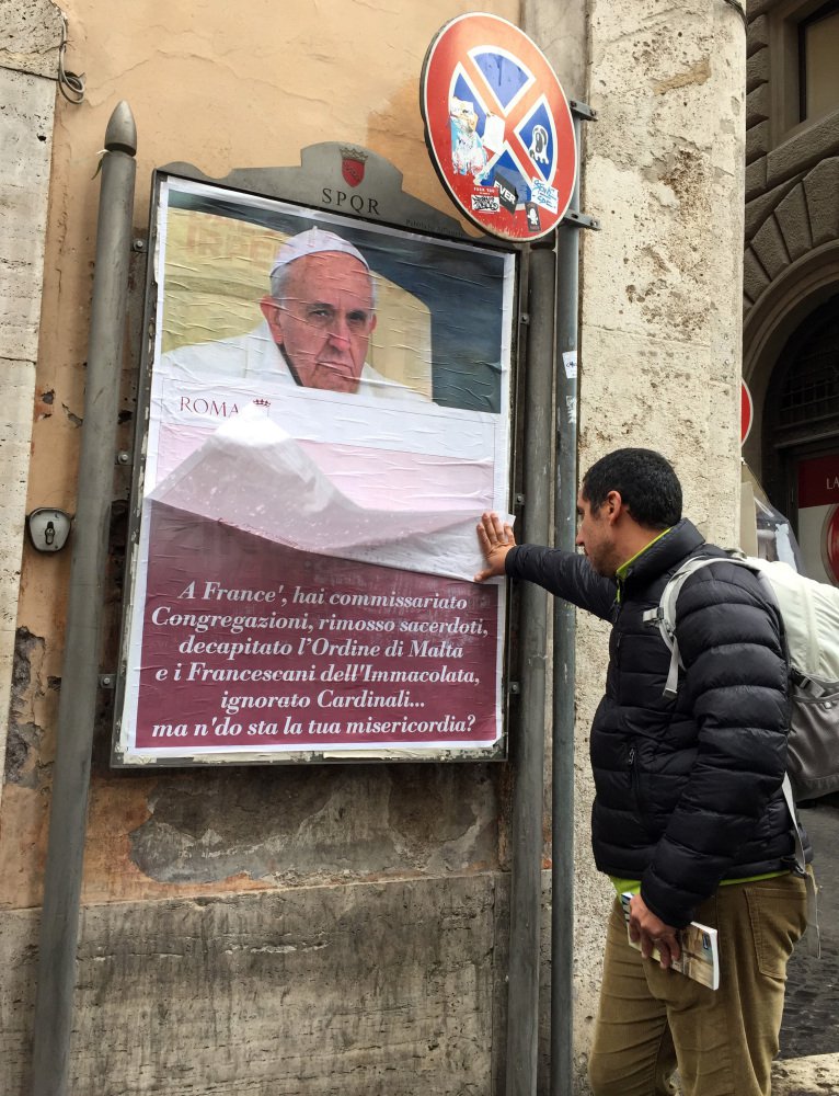 A passerby lifts a paper sheet covering an anti-Pope Francis poster to read it, in central Rome, Saturday, Feb. 4, 2017. On Saturday, posters appeared around Rome featuring a stern-looking Francis and questioning "Where's your mercy?" It referenced the "decapitation" of the Knights of Malta, Cardinal Raymond Burke's marginalization and other actions Francis has taken against conservative, tradition-minded groups. (AP Photo/Beatrice Larco)
