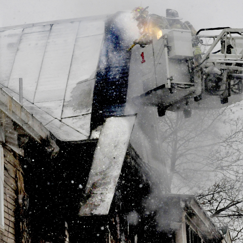 Firefighters working from a ladder truck pull off roofing material to put out a fire that severely damaged an apartment building early Wednesday morning on Summer Street in Waterville.