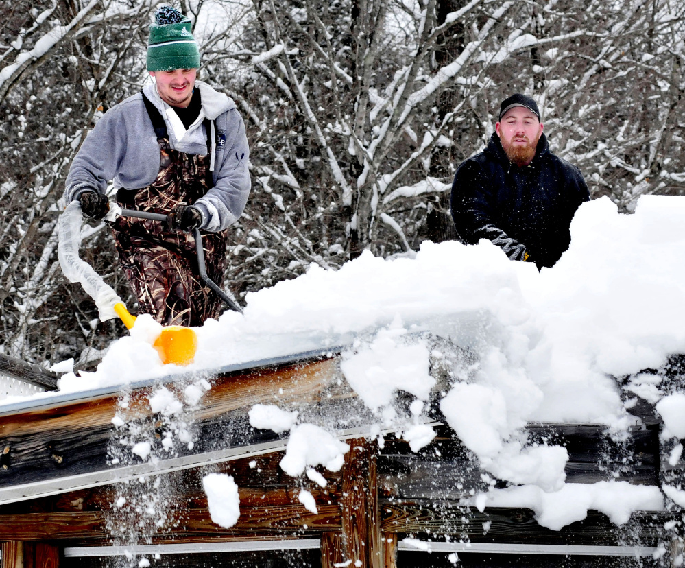 Jake Boivin, left, and Chad Merrill use snow scoops to clear deep snow from a rooftop in New Vineyard on Sunday.  "With 2 feet of snow coming tomorrow, I figured I better shovel this off," Merrill said.