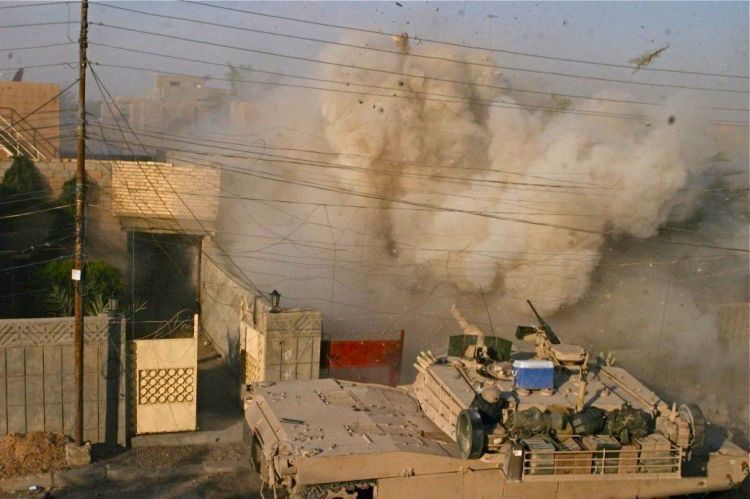 An M1A1 Abrams tank (in foreground with ice chest on top) with the 2nd Tank Battalion fires into a building that Marines received fire from during a battle in Fallujah in 2004. 