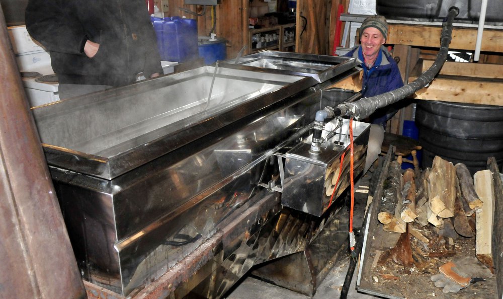 As steam rises from a wood-fired evaporator, John Ackley loads more wood while boiling maple syrup Monday at the Chez Lonndorf sap house on Burrill Hill Road in Skowhegan in preparation for the Maine Maple Sunday event this weekend.