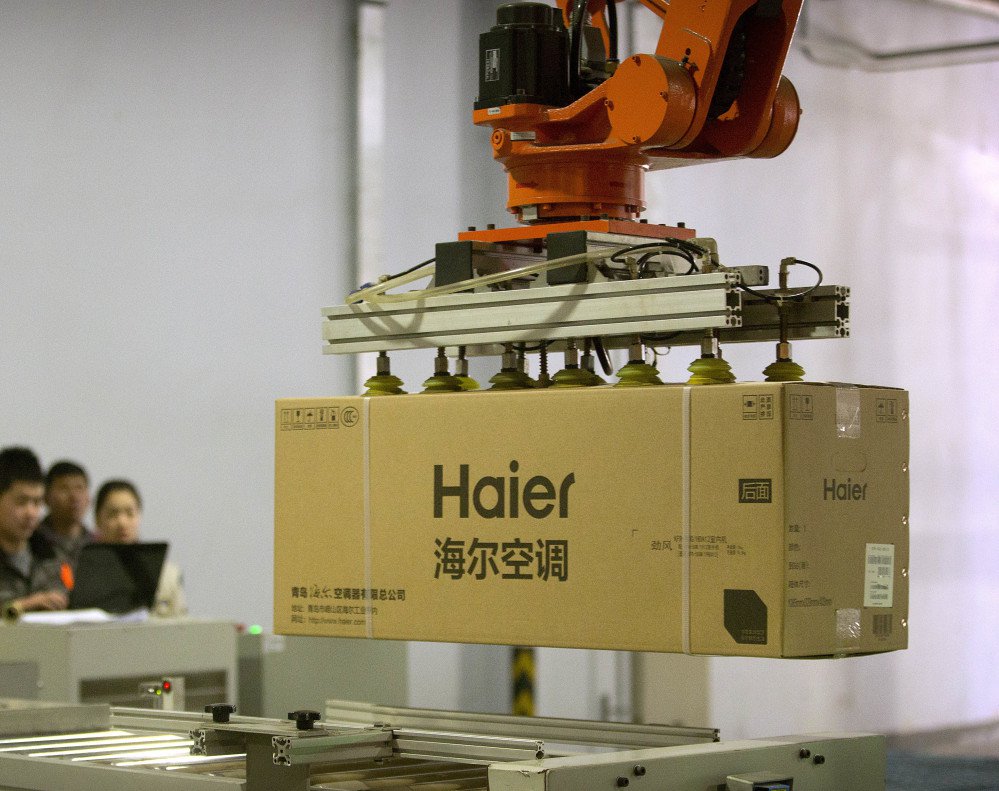 Factory workers watch a machine use suction to lift a box containing an air conditioner at a Haier factory in eastern China. Haier is now the biggest maker of major appliances.