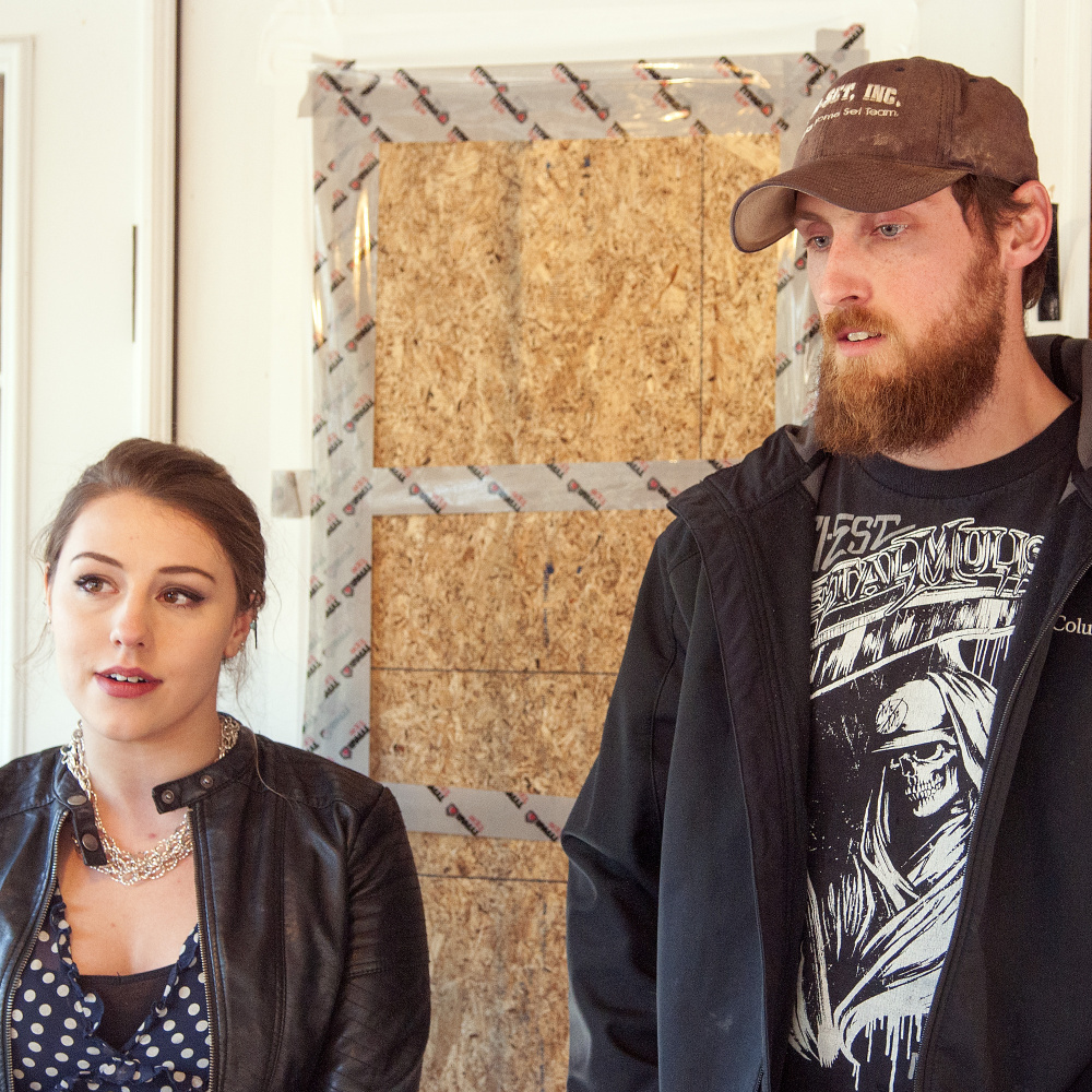 Standing in front of the boarded-over broken window of their front door, Lindsey Levasseur, left, and Trevor Whitney tell the story of an early morning home invasion that happened Wednesday at their home in Richmond.