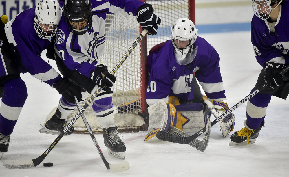 Waterville forward Zack Menoudarakos (7) battles for the puck with Hampden defenseman Jacob Weston as Hampden goalie Cole Benner looks on during a Class B North quarterfinal game last Saturday in Waterville.