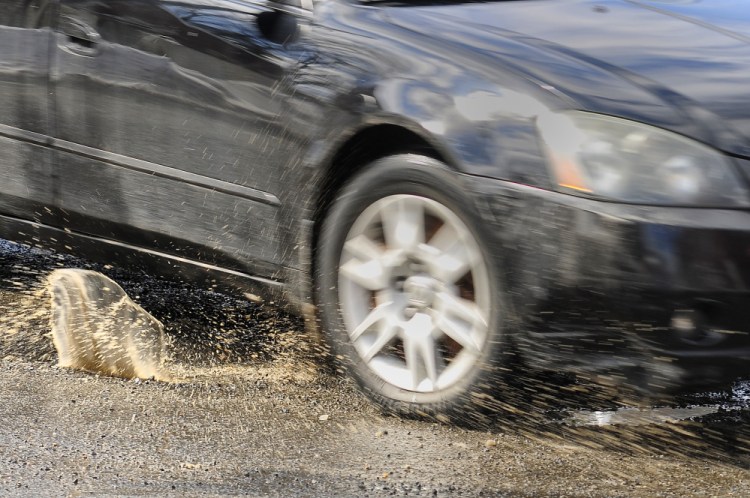 A car splashes through a pothole Wednesday at the corner of Water and Bridge streets in Gardiner.