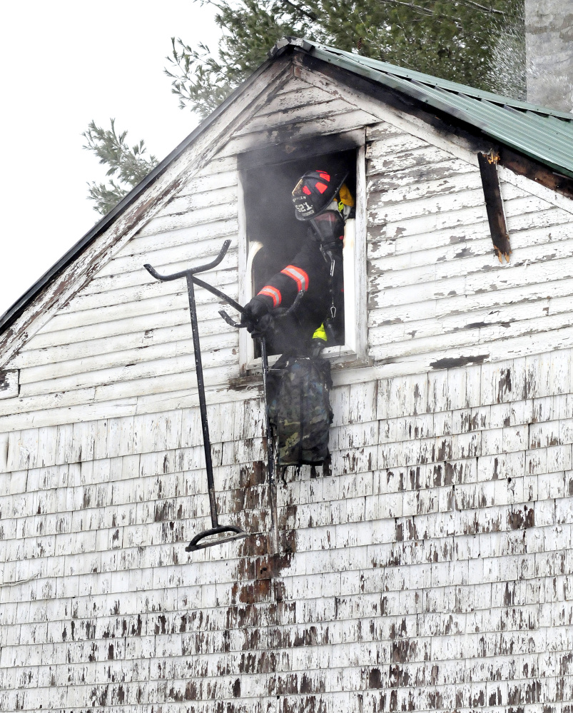 A firefighter throws burned items out a second-story window where fire destroyed a home Friday on Barker Road in Troy.