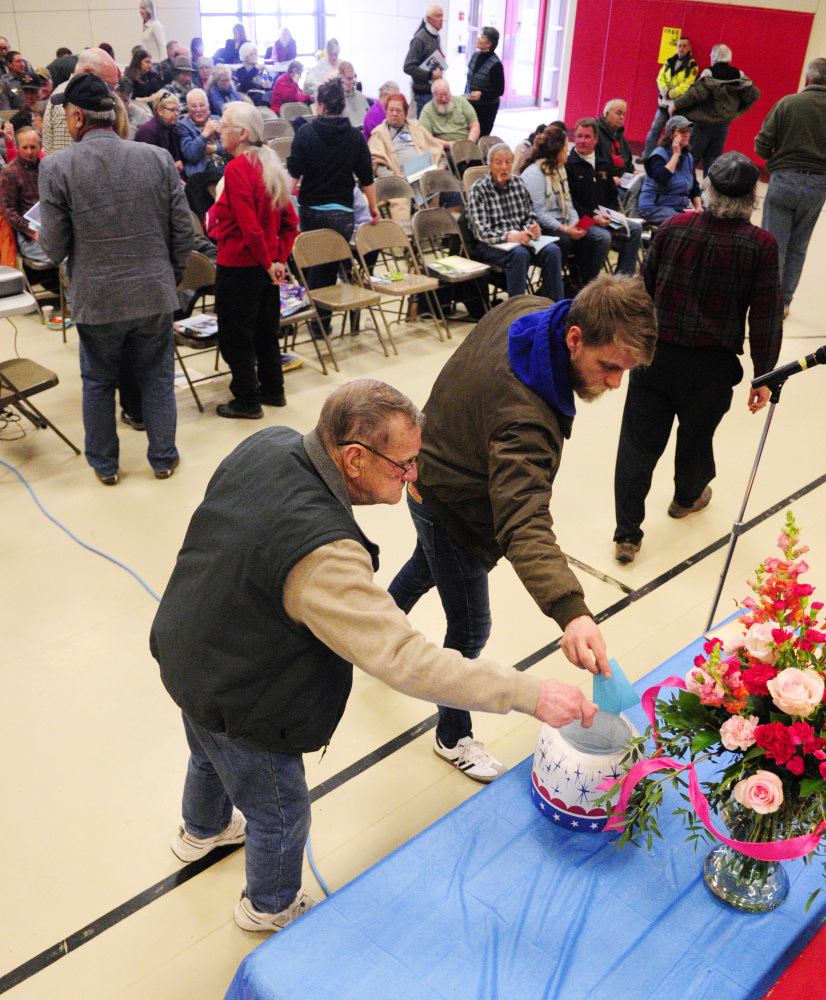 Residents put paper ballots into a container to vote Saturday during the China Town Meeting in the China Middle School gymnasium.