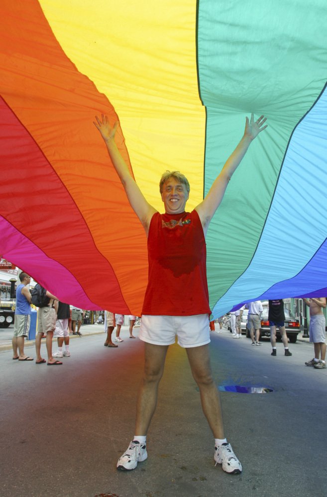 In 2003, Gilbert Baker stands in Key West, Fla., under a 1¼-mile-long rainbow flag that stretched across the island city from the Atlantic Ocean to the Straits of Florida.