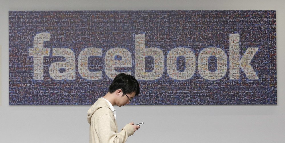 A man walks past a Facebook sign in an office on the Facebook campus in Menlo Park, Calif. Facebook announced Thursday it is launching a tool to help users spot false news articles on the site. The tool will be available to users in 14 countries, including the United States.