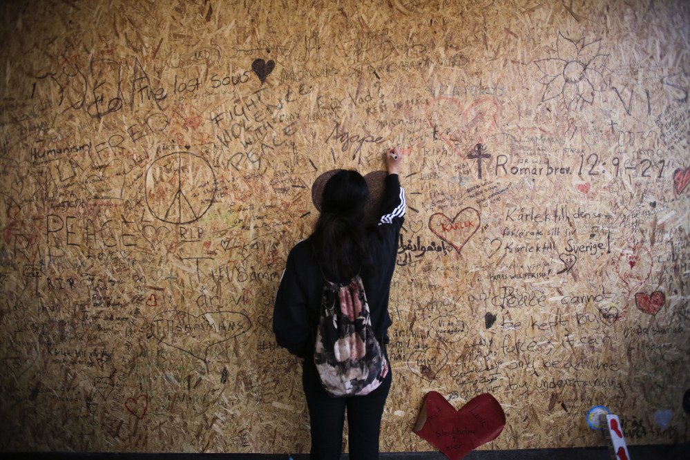 A woman writes a message on a wooden board Sunday at the Ahlens department store in Stockholm, Sweden, where the hijacked truck crashed Friday. Four people died in the rampage and 10 of the 15 people injured remained hospitalized Sunday, including one child.