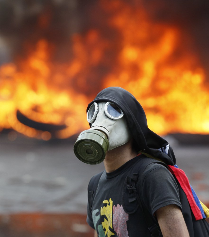 An anti-government activist standing in front of burning barricade is one of thousands protesting in Caracas, Venezuela, on Monday.