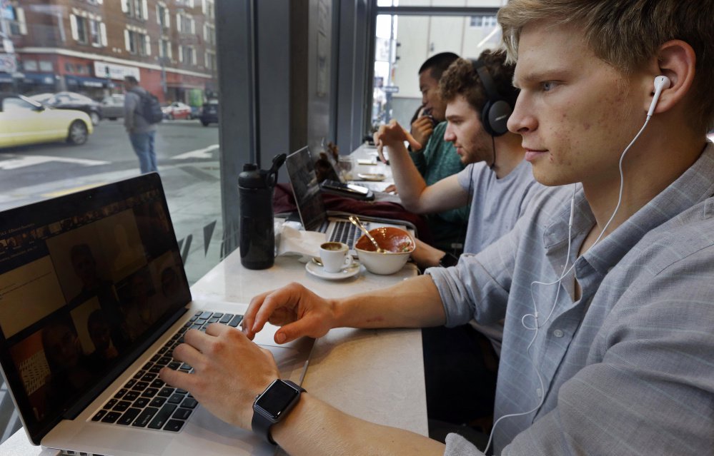 Connor Mitchell, right, works on a computer at a cafe in San Francisco. With college costs rising steadily and with more courses available free online, some observers are beginning to question the need for traditional college.