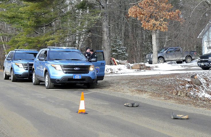 Two Maine State Police troopers consult outside a residence on Winnecook Road in Burnham while investigating the death of Joyce Wood on Sunday. A pair of boots lie in the road in foreground.