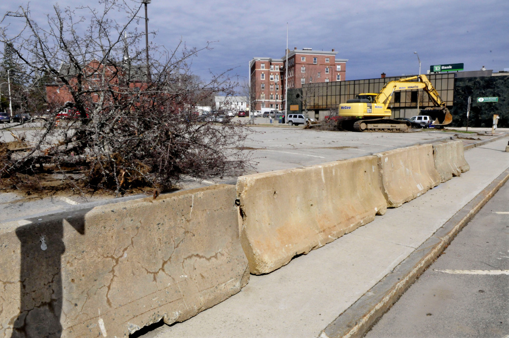Concrete barriers were placed around the site where construction on the Colby College multi-use residential building is beginning in The Concourse in Waterville Monday. In the background an excavator rips a live tree from the pavement.