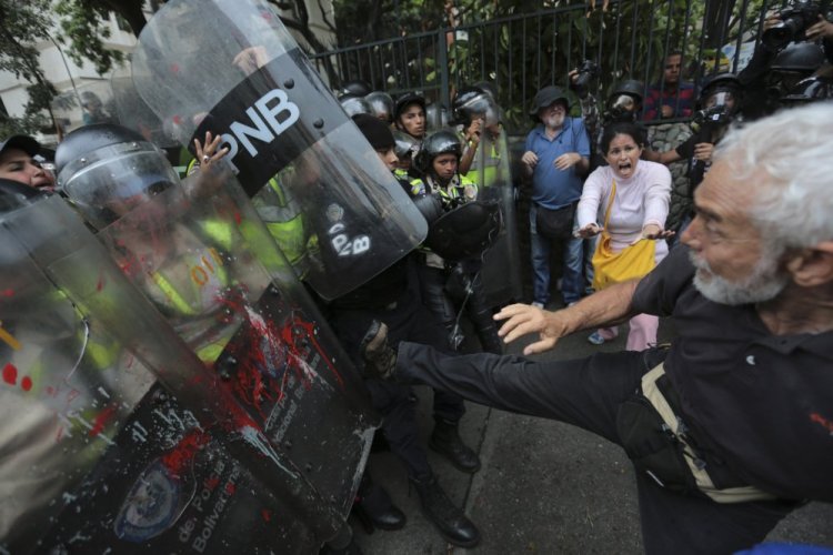 An anti-government protester kicks at riot police blocking a march of elders against President Nicolas Maduro in Caracas, Venezuela, on Friday. The protest billed as the "March of the Grandparents" comes after six weeks of political unrest.