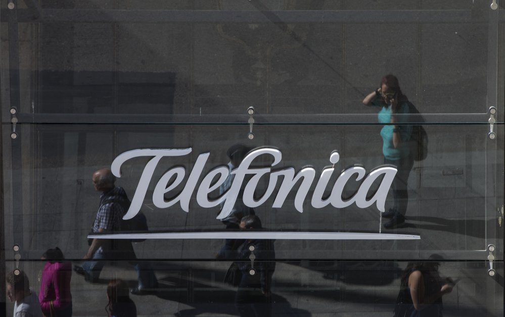 People are reflected in a glass sign of a Telefonica building in Madrid, Spain, on Saturday. The government said several companies including Telefonica had been targeted in a ransomware cyberattack that affected the Windows operating system of employees' computers.