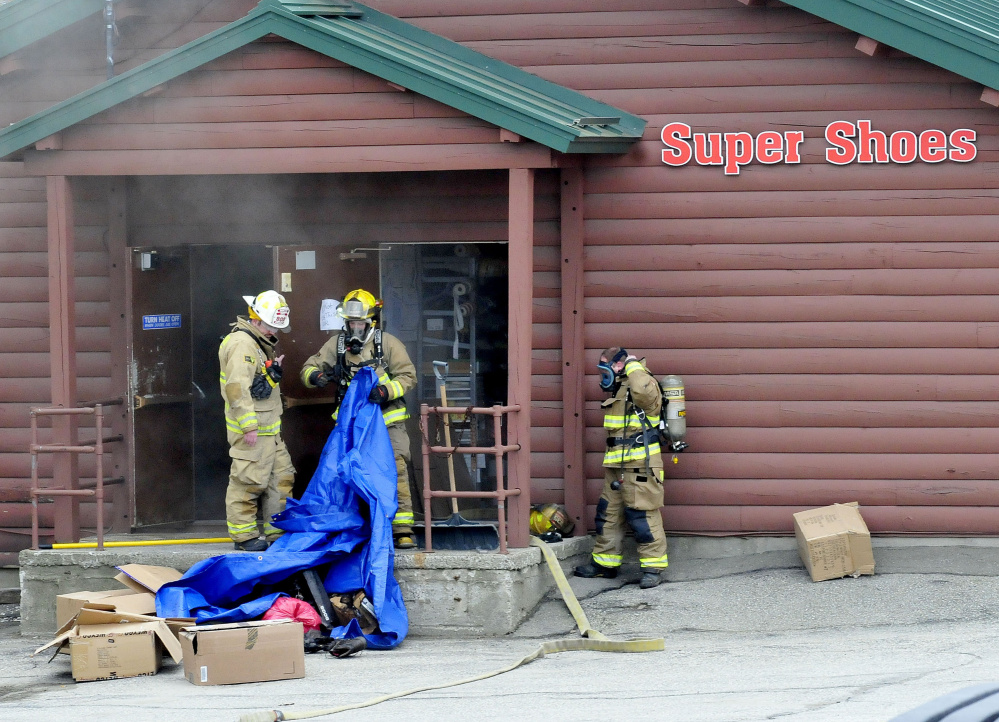 Waterville firefighters carry a tarp full of smoldering shoes and footwear out of the Super Shoes store in Waterville after a fire was reported on Tuesday.