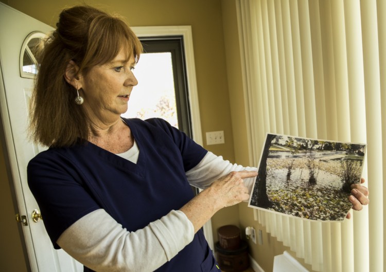 Jacquelyn Cyr of Windsor Avenue in Augusta on Wednesday holds a photo she took of standing water in her yard.