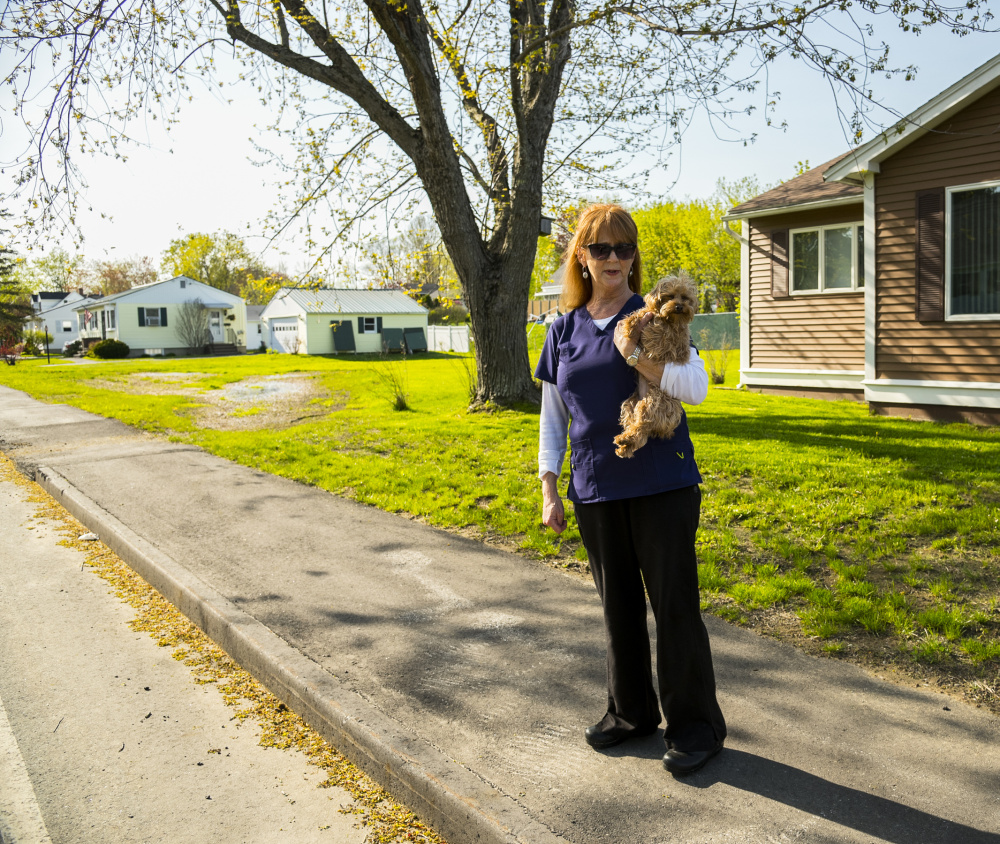 Jacquelyn Cyr of Windsor Avenue in Augusta stands with her dog Poppy on Wednesday on a new sidewalk in front of her house. She said that the sidewalk, which was replaced two years ago, is causing standing water on lawns in her neighborhood.