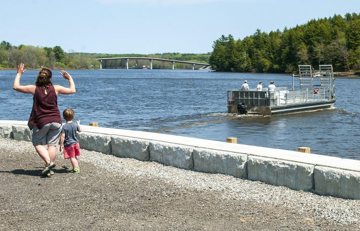Liz Dunn, left, and her son Spencer, 3, of Lyman, wave to the staffers on the Swan Island Ferry from the recently rebuilt parking lot Wednesday on the shore of Kennebec River in Richmond. They'd just returned from a visit to the island.