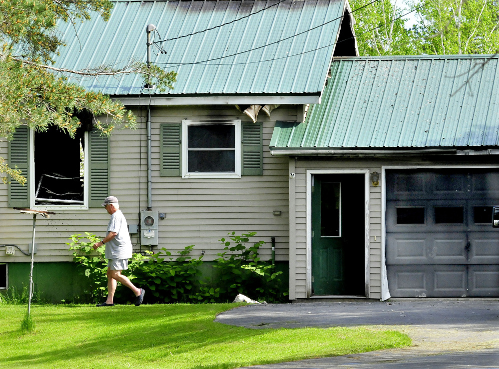 A man walks past burned-out windows and damaged doors at Sumner "Bud" Jones' home on Peltoma Avenue in Pittsfield after a fire there Tuesday.