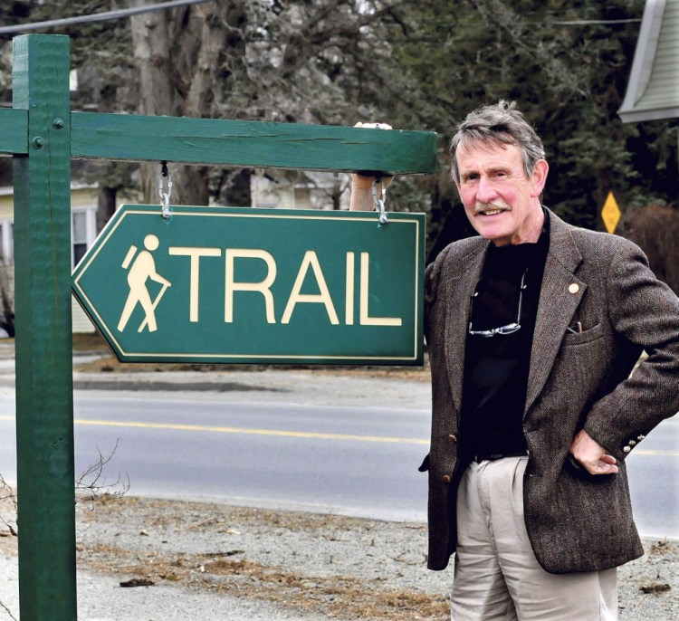 Peter Garrett, a director of the Kennebec Messalonskee Trails organization, beside a sign along the 40-mile network of trails in 2014, invites surrounding communities to take part in the annual National Trails Day walk on Saturday in the spirit of cooperation and civility.