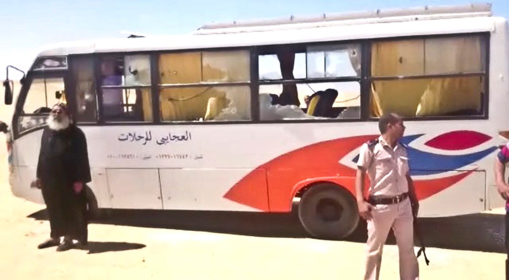 A policeman and a priest stand next to a bus after it was stormed by gunmen in Minya, Egypt, on Friday. Egyptian officials say dozens of people were killed and wounded in the attack on a bus carrying Coptic Christians, including children, south of Cairo. 