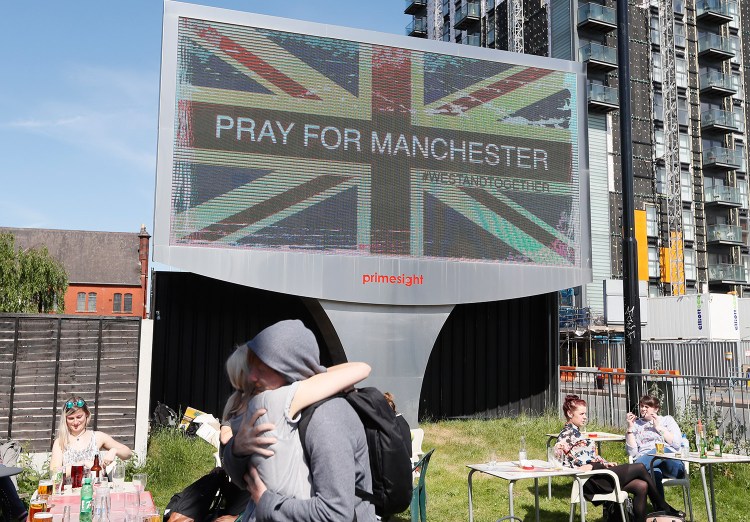 A couple embrace under a billboard in Manchester city center on Tuesday, the day after the suicide attack at an Ariana Grande concert that left at least 22 people dead.