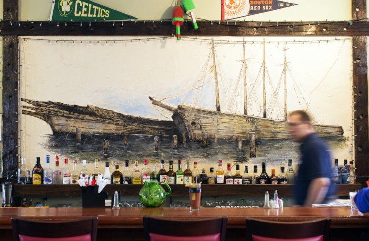 A mural of schooners Hesper and Little Luther is framed with wood from the ships after they were dismantled. It hangs behind the bar at the Twin Schooner Pub, which is tended by Greg McAllister.