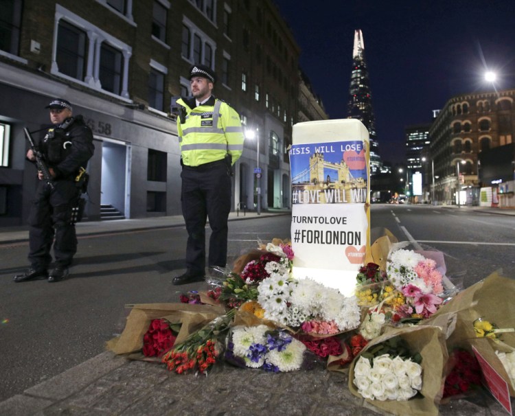 Police officers stand guard next to floral tributes in London near the scene of Saturday's attack by men who rammed some people with a van and stabbed others.
