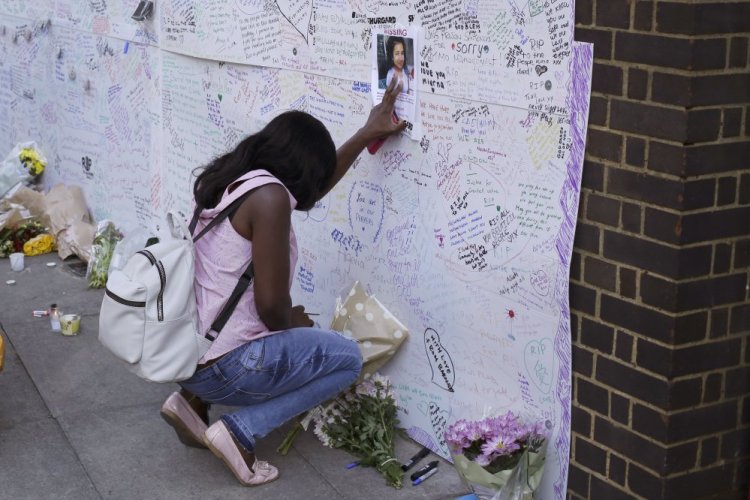 A woman touches a missing poster for 12-year-old Jessica Urbano on a tribute wall after laying flowers on the side of Latymer Community Church next to the fire-gutted Grenfell Tower in London on Friday.