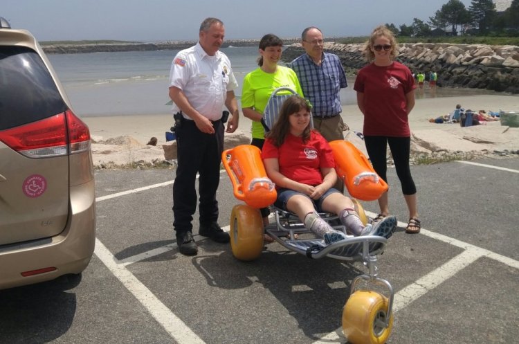 Smile Mass co-founder Susan Brown, second from left, presents a donated floating wheelchair to, from left, Wells Fire Chief Wayne Vetre, Town Manager Jonathan Carter and lifeguard captain Emily Bordeau. Kristen Brown is seated in the wheelchair
.
Photo courtesy of Linda Rizzo
