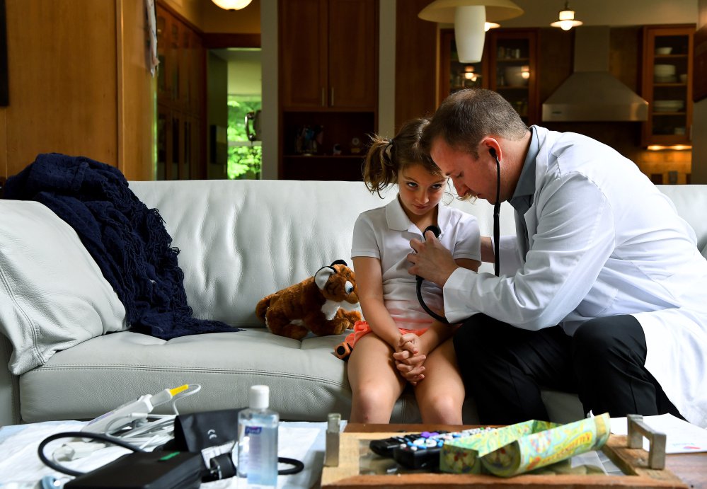 Claire Bennett, 8, watches as Dr. Adam Lowry examines her at her family's home in Great Falls, Va. The girl needed a last-minute physical for summer camp.