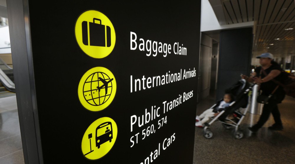 A woman pushes a stroller near a sign for international arrivals Monday at the Seattle-Tacoma International Airport. The U.S. Supreme Court said Monday that President Trump's travel ban on visitors from Iran, Libya, Somalia, Sudan, Syria and Yemen can be enforced if those visitors lack a "credible claim of a bona fide relationship with a person or entity in the United States."